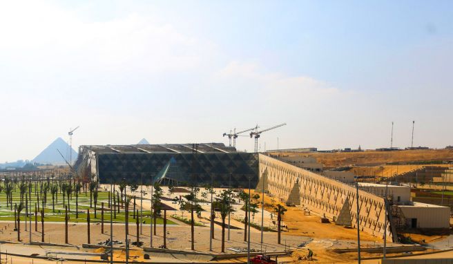 Das Große Ägyptische Museum wird ein kolossales Bauwerk. Hinter ihm sieht man die Pyramiden von Giseh auf einem Plateau.