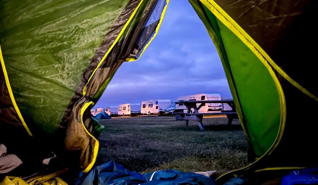 Aus dem Zelt blickt unsere Autorin auf ein typisches Campingplatz-Ensemble: Picknicktisch, Wohnmobile und andere Zelte.